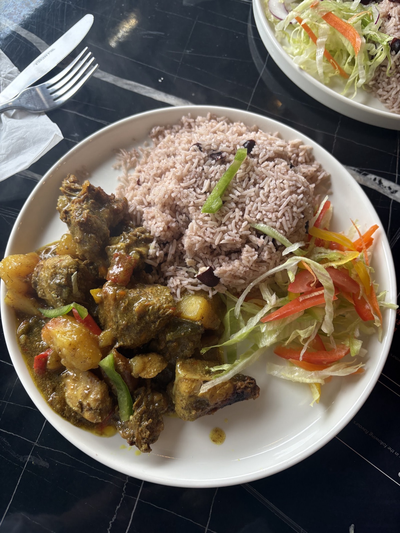 A plate of Jambay Kitchen curry goat with rice and peas, fresh salad and vegetables