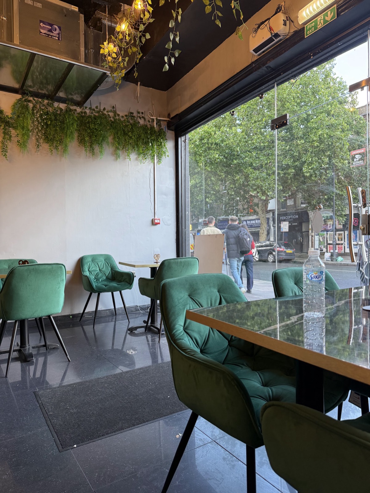 Inside Jambay Kitchen — green velvet chairs and hanging plants by the window onto Stoke Newington Road